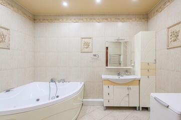 bright bathroom features a corner bathtub, a vanity with mirror, and a tall cabinet. The walls are...