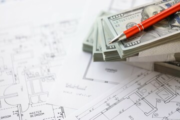 Big amount of US dollars money bills with pen and planning blueprints of residential building...