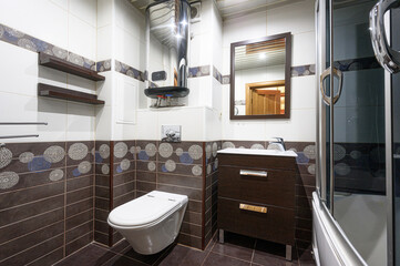 Cozy bathroom with brown and white tiles, a toilet, sink cabinet, and a water heater. A mirror reflects an open door
