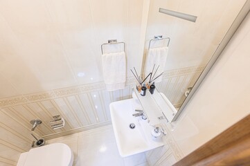 high-angle shot shows a bathroom with a sink, mirror, towels, and toilet. The walls are tiled in...