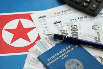 North Korean won money bills lies on table with pen, calculator, passport and tax forms