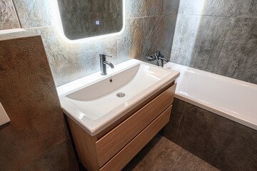 Modern bathroom with a white sink vanity, lighted mirror, and gray tile walls. Clean and contemporary design