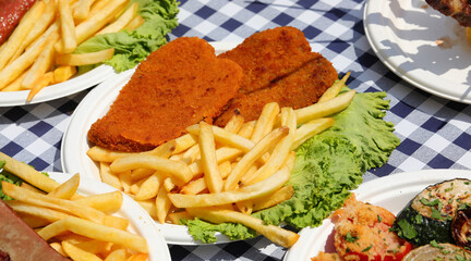 cutlets and french fries in the dish on the table with a bed of green lettuce leaves at the village festival
