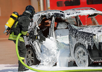 Firefighter with helmet and oxygen cylinder while spraying   foaming coat to extinguish   fire of   crashed vehicle without a doorman after   road accident
