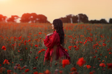 Beautiful girl with black hair and short red dress posing in poppy field of flowers.