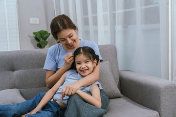 Fototapeta premium An Asian mother and daughter sit together indoors, smiling and bonding over a book, enjoying digital learning and joyful family time.