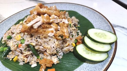 Yang Chow Fried Rice with Peas, Corn, Chili and Carrots and toppings of crispy fried chicken and cucumber slices, served on banana leaves.