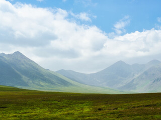 Serene vista of vibrant green pastures gently sloping towards imposing, dark mountain peaks. Nature's majestic beauty.