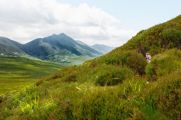 Grassy hillside shows a view of the Strickeen Mountain range under a cloudy sky. Rolling hills stretch into the distance, Ireland.