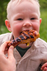 Laughing toddler outdoors with grilled chicken drumstick at picnic