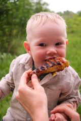 Laughing toddler outdoors with grilled chicken drumstick at picnic