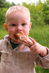Laughing toddler outdoors with grilled chicken drumstick at picnic