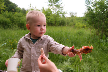 Laughing toddler outdoors with grilled chicken drumstick at picnic