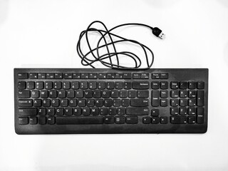Top view of a black wired USB keyboard with numeric keypad, coiled cable, and white background,...