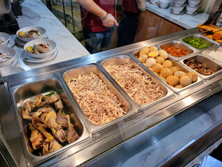 Assorted chicken, eggs, herbs, and toppings displayed in a stainless steel food warmer at a...