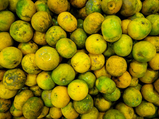 Close-up top view of a pile of fresh green-yellow oranges with natural blemishes, stacked in a...