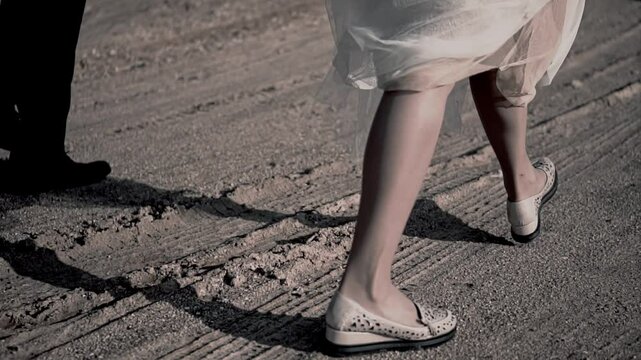 A man and a woman holding the hem of their dress in their hands are walking along a dirt road. Shooting in slow motion