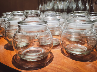 Rows of empty round glass jars with lids displayed neatly on a wooden surface, reflecting light and showcasing clean design, storage utility, and kitchen organization.