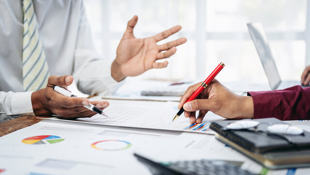 Two men are sitting at a table with a red pen and a white shirt