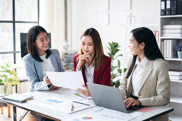 Three women are sitting at a table with papers and laptops
