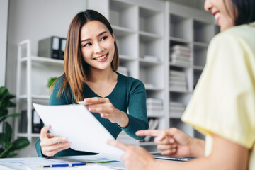 Two women are sitting at a desk with a white piece of paper in front of them