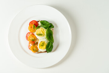 Light snack with a sandwich. Sandwich with chicken eggs, tomatoes and spinach. Sandwich on a white plate. Isolated.