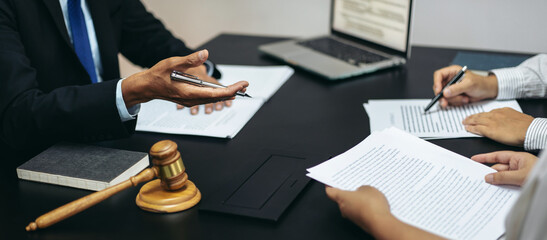 Three people are sitting at a table with legal documents and a gavel