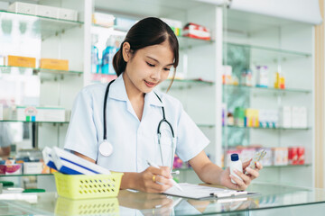 A woman doctor is writing on a clipboard while looking at her phone