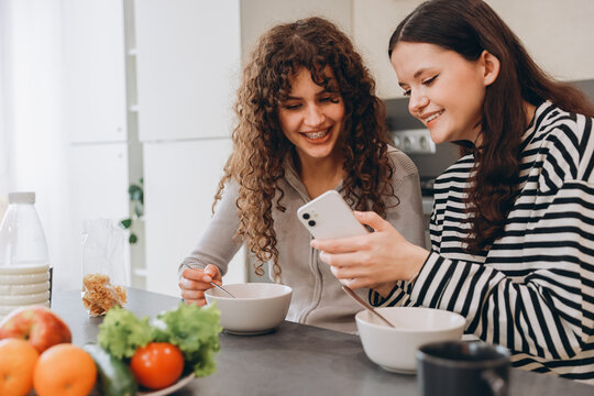 Teen girls having breakfast and looking at smartphone
