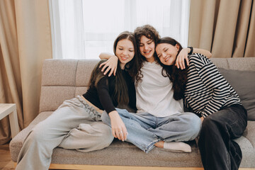 Teenage girls embracing on sofa, enjoying friendship and home comfort