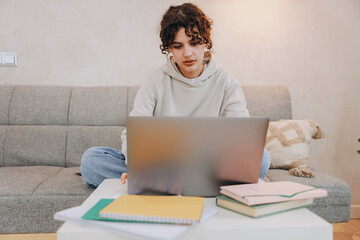 Teen student girl studying using laptop sitting on sofa at home