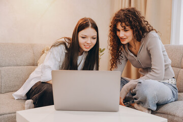 Two teenage girls studying together using laptop at home