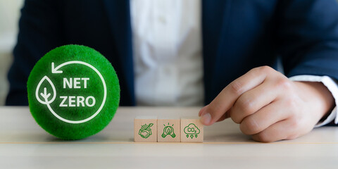 Net Zero, sustainable business strategy concept. Hand arranging wooden blocks with sustainability icons with green sphere labeled "Net Zero". Corporate commitment to environmental responsibility.