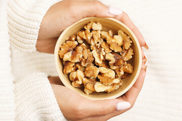 Hand holding walnut kernels. Healthy organic snack in wooden bowl. Natural plant-based protein. Crunchy dried fruit in cozy setting. Balanced food for diet and wellness. Vegetarian energy source.