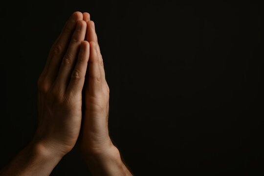 Close-up of male hands clasped in prayer against a dark background, a concept for faith, spirituality, hope, and meditation.