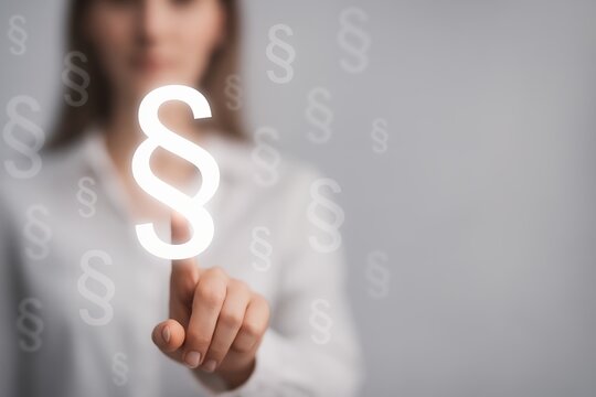 Woman's finger pointing at a glowing paragraph symbol on a transparent background, surrounded by smaller paragraph symbols; concept for legal, law, justice, and digital technology.