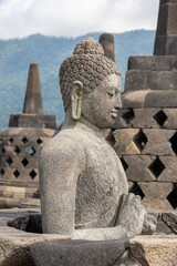 Closeup profile view of ancient Vairocana buddha statue in situ with stupas in background at historic Borobudur, Magelang, Central Java, Indonesia