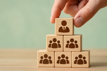 Hand placing wooden block with a business person icon on top of a pyramid of blocks representing a team, concept for business management and human resources