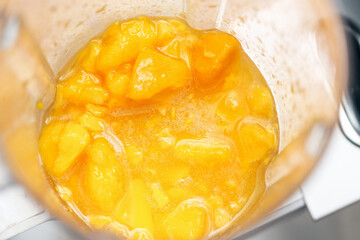 Blended mango smoothie in blender. Thick yellow fruit pulp. Closeup of healthy tropical drink...
