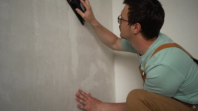 Professional handyman sanding plastered wall with sandpaper, carefully smoothing surface for optimal painting preparation, ensuring precise and polished renovation results