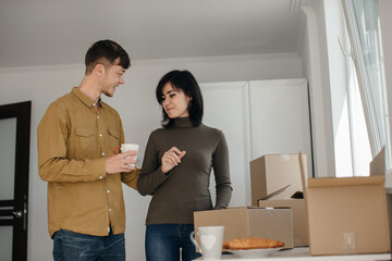 Young couple moving into new home, drinking coffee and unpacking boxes