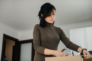 Woman packing cardboard box using packing tape while moving house