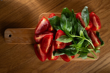 Freshly sliced tomatoes and basil leaves are arranged on a wooden cutting board, ready for culinary...