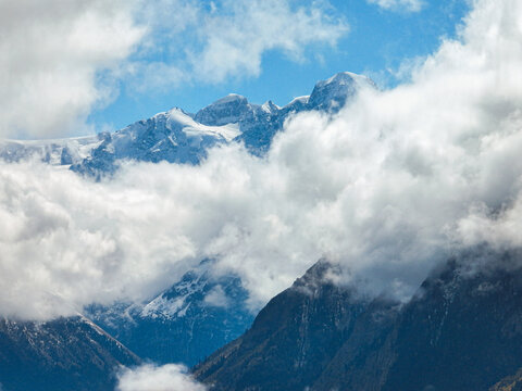 Close up view of majestic snow-capped mountains partially hidden by fluffy white clouds against a blue sky - Powered by Adobe
