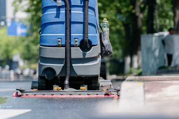 Workers are cleaning the road with a floor scrubber