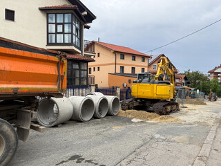Excavator and concrete pipes at residential roadwork site. Urban infrastructure repair in progress...
