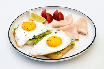 Avocado Toast with Fried Eggs, Turkey Ham, Lemon, and Tomato Slices on a Breakfast Plate