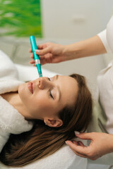 Vertical shot of professional beautician performing microneedling treatment with dermapen on female...