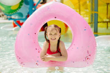 Smiling girl relaxing on pink float in water park pool