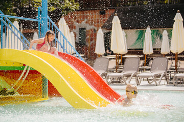 Children sliding down into waterpark pool on sunny day